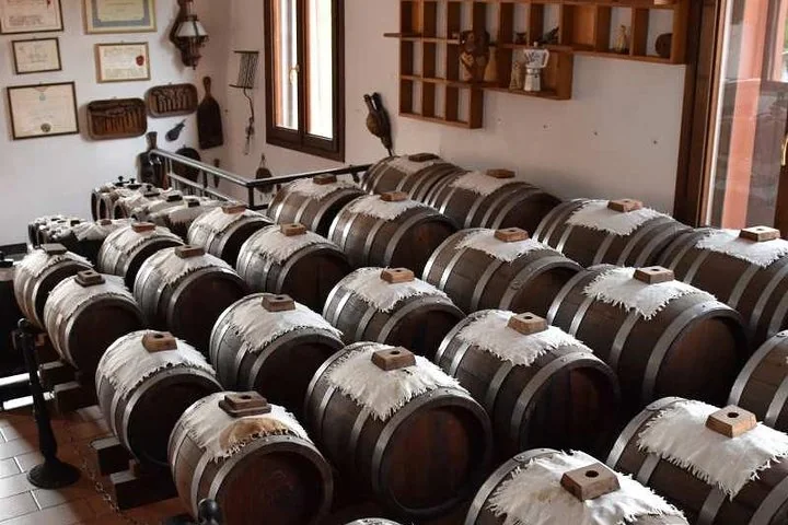 Rows of small wooden barrels with cloth-covered bungholes in an attic room with framed certificates on the walls