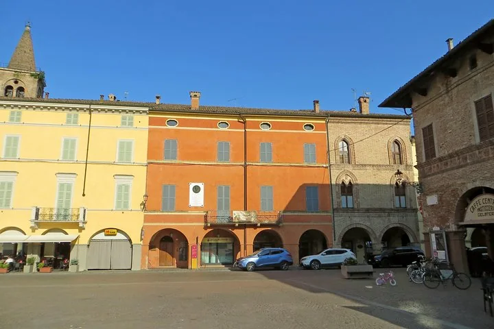 Palazzi porticati colorati in giallo e arancione su una piazza soleggiata, con un campanile a sinistra