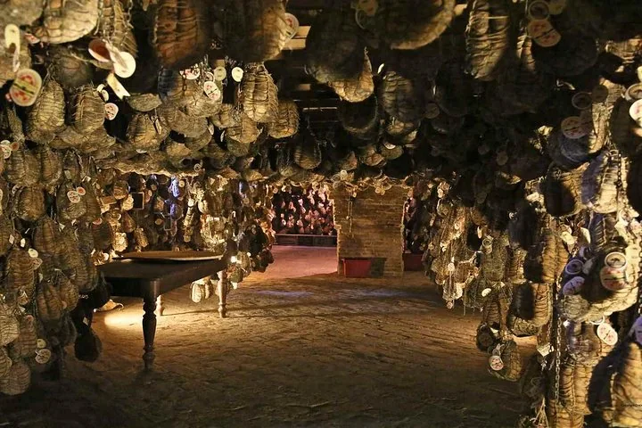 A low, lamplit cellar with hundreds of tagged, string-tied culatelli hanging around a wooden table