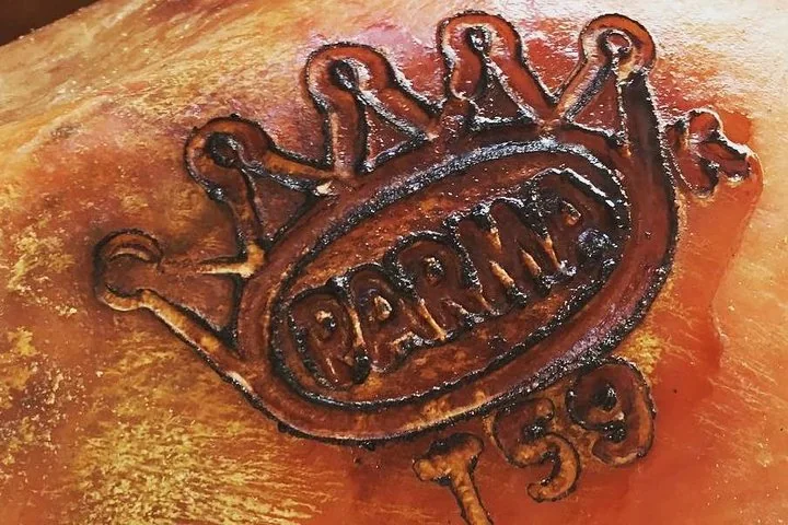 Close-up of a crown-shaped brand reading PARMA burned into the golden rind of a ham