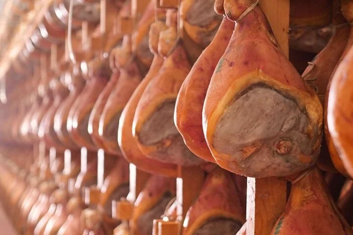 Rows of whole cured hams hanging from wooden racks in a curing room