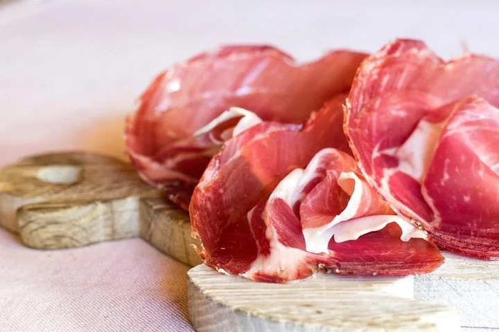 Thin folded slices of deep red cured meat on a round wooden board