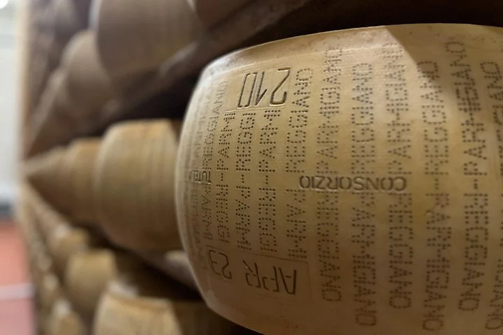 Close-up of a Parmigiano Reggiano wheel on a shelf, its rind dotted with the words PARMIGIANO REGGIANO and a month code