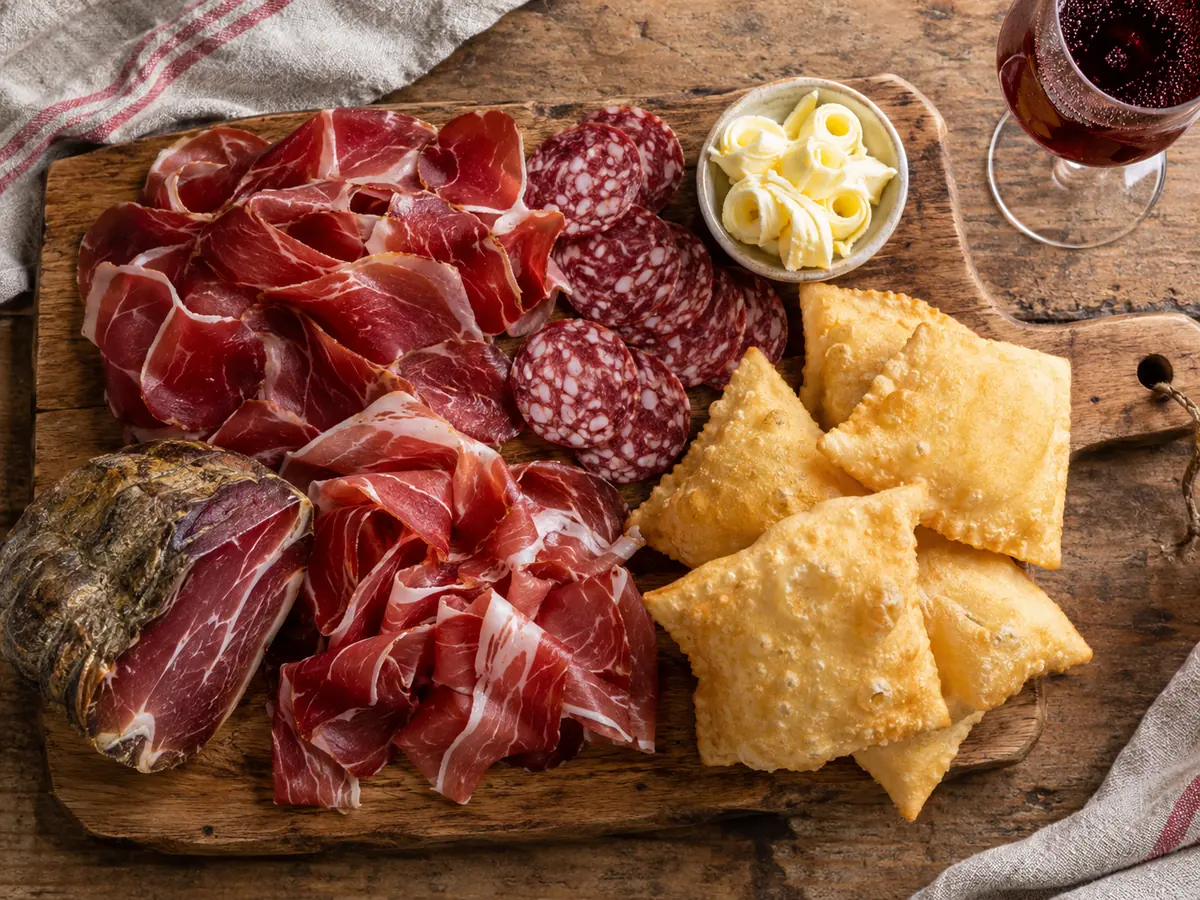Une planche de charcuterie finement tranchée, salami, copeaux de beurre et pâte frite avec un verre de vin rouge